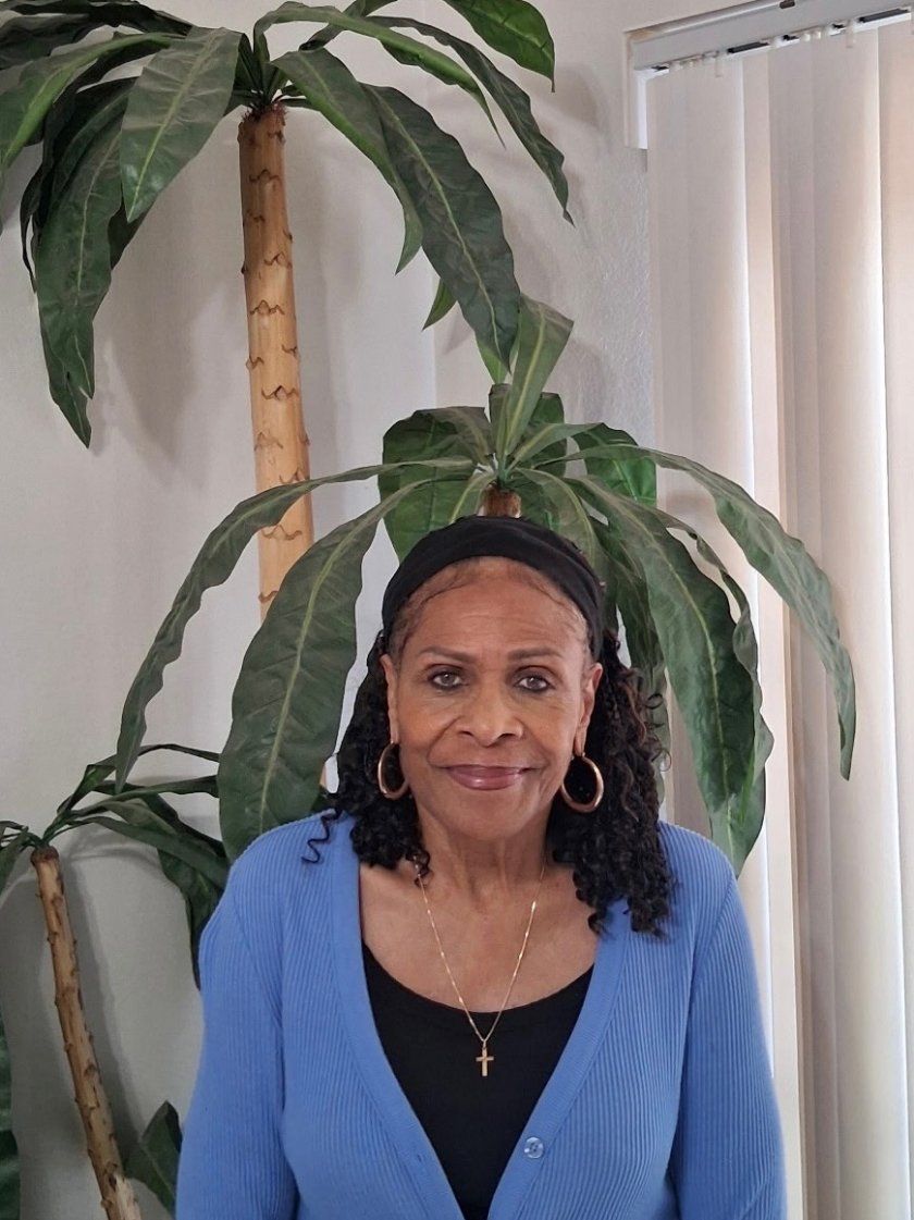 Patricia Woods, owner of Integrity Bookkeeping Service, smiling in a blue cardigan among leafy plants